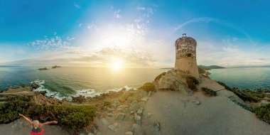 tourist woman hiker walking on top in Punta Parata by the Sanguinaires islands. Sunset aerial view of Parata tower in Corsica island of France. Ancient Genoese tower in Corsica. 360 degrees panorama.