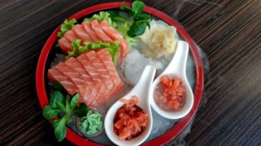 Raw pieces of Salmon sashimi cutting fresh in a Japanese food style restaurant. Flat lay top view on a salmon sashimi dish with ginger and wasabi and vegetable on a wooden table. Japanese fusion food