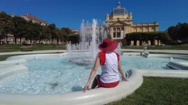 Girl with hat relaxing in the fountain of the Art pavilion of 1898 of King Tomislav Square. City park of Zagreb capital of Croatia in Europe. Lenuci Horseshoe, Lower Town district.