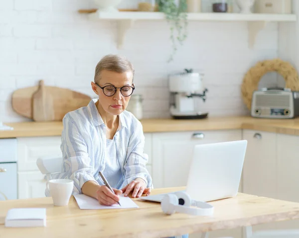 Concentrated senior woman writer typing something on laptop while working online from home