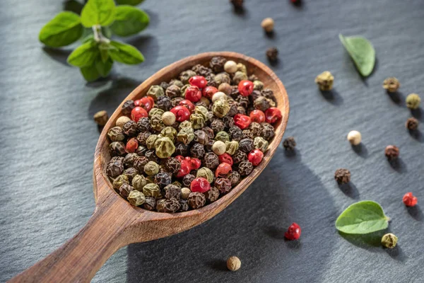 Peppercorns seeds of different colors in wooden spoon closeup, black background — Fotografia de Stock