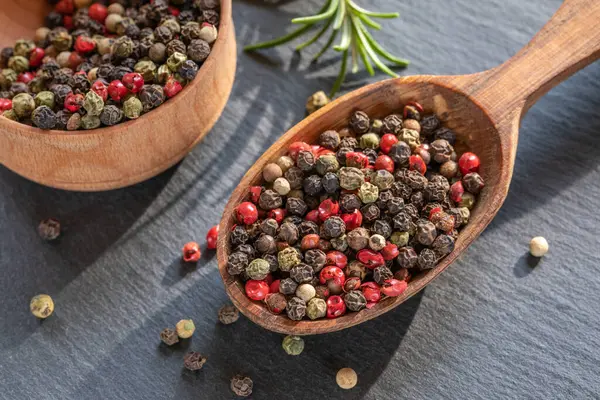 Pepparkorn frön av olika färger i trä sked närbild, svart bakgrund — Stockfoto