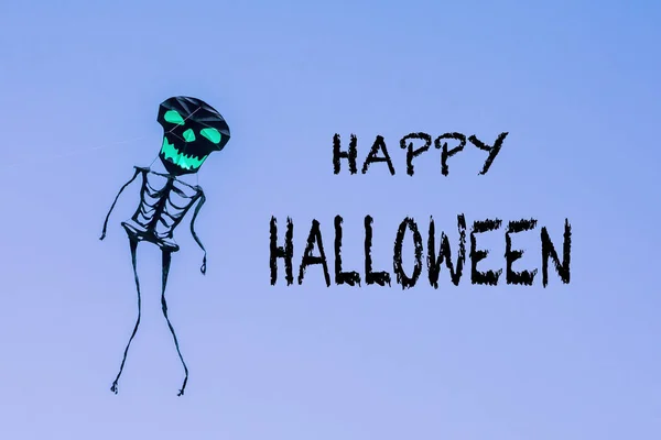 Happy Halloween greeting card. Holiday composition with text Happy Halloween, with skeleton kite on blue background. Postcard for holiday. Spooky concept. Halloween concept. High quality photo