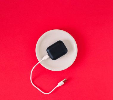 Kablosuz kulaklıklar beyaz seramik tabağa konur. Asgari eğlence konsepti, pastel parlak kırmızı arkaplan üzerine düz konum