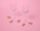 Sklenice na víno a zátky na pastelové růžové pozadí. Horizontální složení, minimální retro styl těší víno koncepce