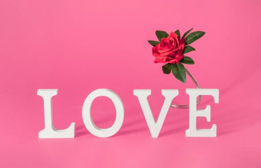 Aşk kelimesi ahşap harflerle kırmızı gülle yazılmış. Pastel pembe arka planda yatay kompozisyon. Minimum Romantik Sevgililer Günü veya Uluslararası Kadınlar Günü Vintage konsepti