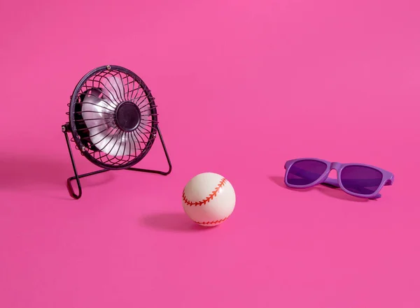 Desk fan, baseball and sunglasses on a pastel pink backgrond. Minimal horizontal composition, summer joy concept