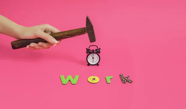 A woman\'s hand holds a hammer above the alarm clock. Minimal horizontal composition on pink background, funny morming waking up before  work stress concept