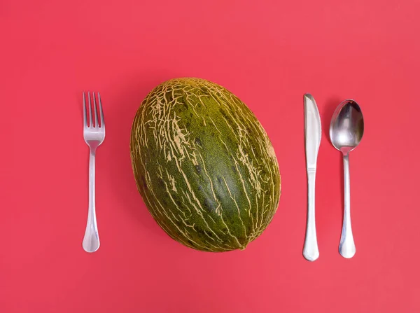 Honeydew melon and cutlery lay down on red background. Minimal horizontal flat lay composition, funny healthy sweet food serving concept