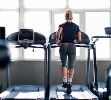 Spor salonundaki koşu bandındaki sarışının arka plan görüntüsü, güç teçhizatı ve sağlıklı yaşam ile egzersiz yapıyor..