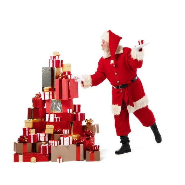サンタクロースは白い背景に隔離されたクリスマスのギフトの大きな山に箱を置く — ストック写真