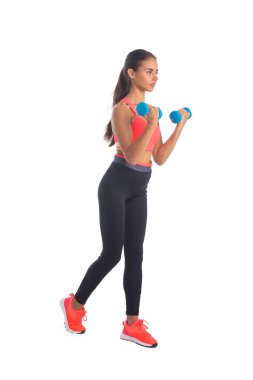 Spor salonundaki kadın tüm vücuduyla ayakta duruyor. Spor salonu kızı elinde dambıl ağırlığıyla stüdyoda beyaz arka planda izole halde duruyor..