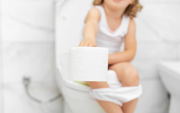 Ребенок в туалете держит туалетную бумагу. — стоковое фото