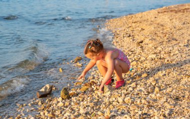 Küçük bir kız deniz kıyısında çakıl taşlarıyla oynuyor.