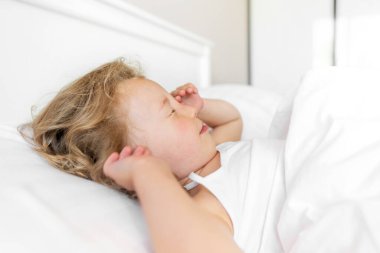 Çocuk uyanıyor ve isteksizce gözlerini ovalıyor..