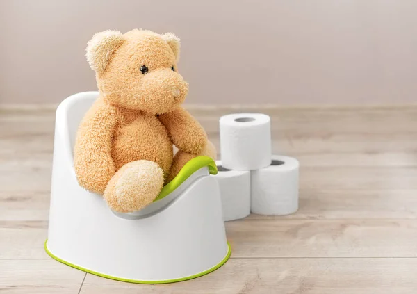 A soft toy sits on a potty. Toilet paper nearby.