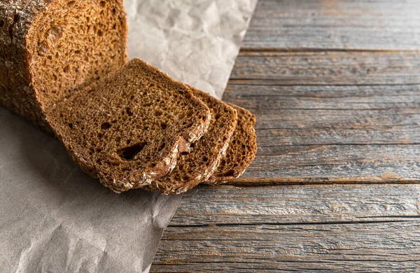 Rye bread with bran on paper and wooden background.