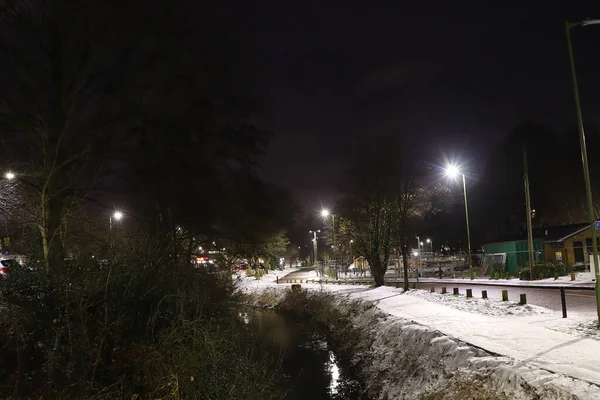 Flowing waters of the river Lea through Hertford in the darkness of winter with bright halogen lights illuminating the way