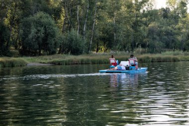 İnsanlar dinleniyor, güneşleniyor, yüzüyor, yazın gölde katamaran kullanıyor..