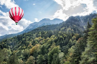 Mavi gökyüzünde sıcak hava balonuyla yüksek Apls Dağları manzarası.