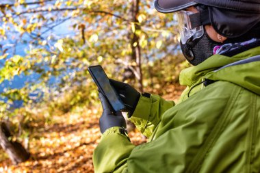 Kauçuk eldivenli bir kadın COVID-19 döneminde ormanda akıllı telefon kullanıyor..