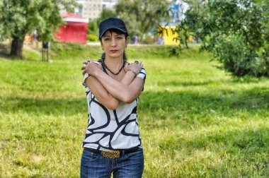 Bahçede duran genç bir kadın Ağaçların ve yeşil çimlerin arkasında.