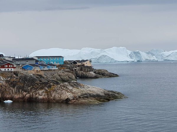 View of colorful houses on the coast of Ilulissat, in the background the ice barrier of the Kanga icefjord
