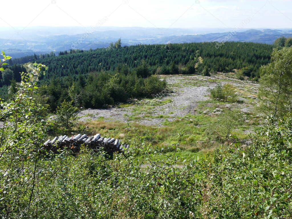 View from the circular path of the Glinge pumped hydroelectric energy storage, North Rhine-Westphalia, Germany, of the mountains and forests of the Sauerland, with a pile of wood in the foreground