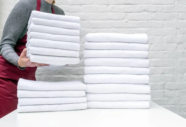 Beyaz masada bir sürü beyaz havlu ve çamaşırhanede ya da beyaz arka planda bir otelde çalışan var.