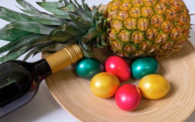 Boyalı paskalya yumurtaları kırmızı yeşil ve altın renkleri, şişe kırmızı şarap ve beyaz arka planda ananas, üst manzara..