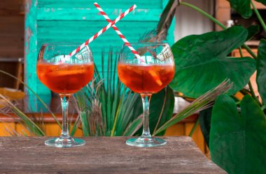 Yeşil arka plandaki eski ahşap masada camda tropikal yapraklarla birlikte Aperol spritz kokteyli..