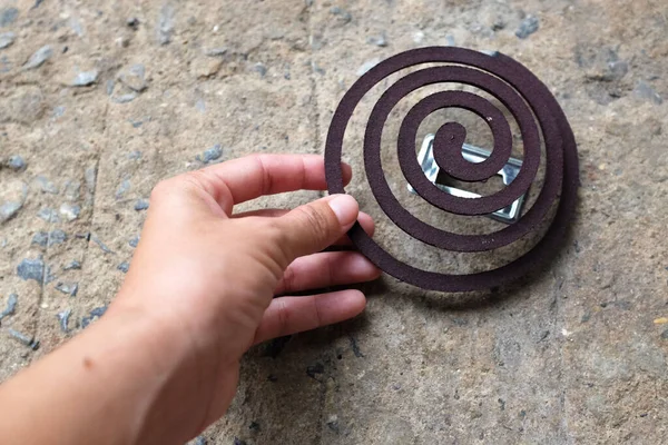 Adamın eli çimento zemininde siyah sivrisinek savar bobini tutuyor.