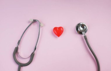 Üst manzara, steteskop ve pembe arka planda kırmızı kalpler. Sağlık hizmeti kavramı.