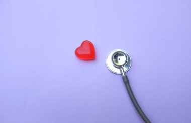 Tıbbi steteskop ve kırmızı kalp, mor pastel arka planda. Kardiyoloji kavramı