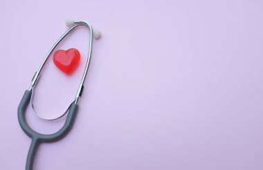 Mor pastel arka planda steteskop ve kırmızı kalpler. Sağlık hizmeti kavramı.