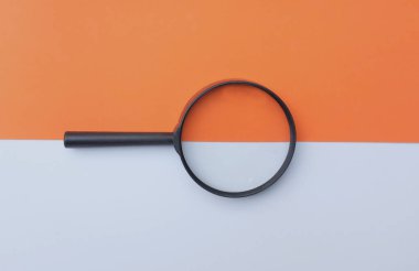 Siyah, renkli kağıt üzerinde büyüteç, beyaz ve turuncu geometrik şekiller.