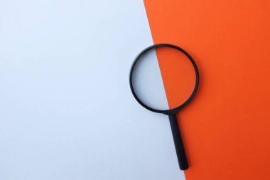 Siyah, renkli kağıt üzerinde büyüteç, beyaz ve turuncu geometrik şekiller.