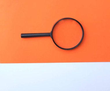 Siyah, renkli kağıt üzerinde büyüteç, beyaz ve turuncu geometrik şekiller.