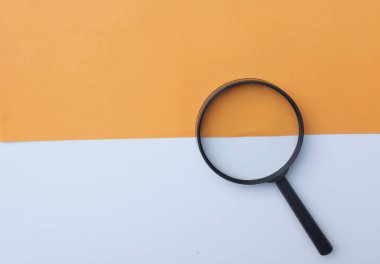 Siyah, renkli kağıt üzerinde büyüteç, beyaz ve turuncu geometrik şekiller.