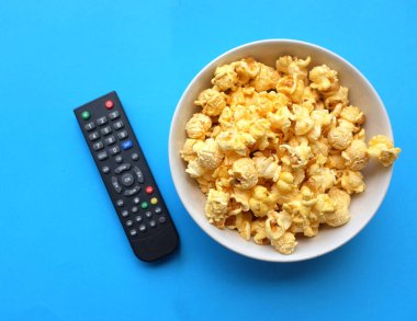 Bir kase taze patlamış mısır ve uzaktan izole edilmiş mavi arka plan.