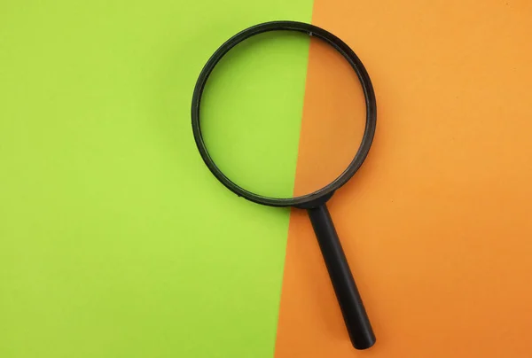 The black a magnifying glass on colored paper orange and green geometric shapes backgrund .minimal creative concept