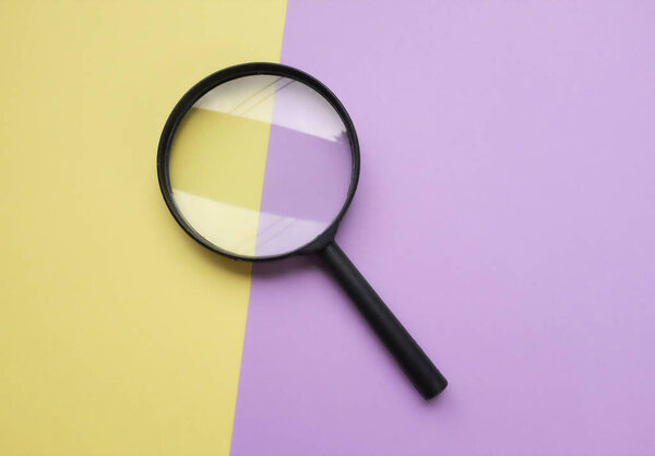 black round magnifying glass on yellow and purple pastel background. used for searching or expanding books.