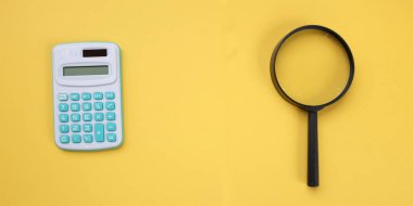 Düz bir hesap makinesi ve siyah bir büyüteç sarı arkaplandadır..