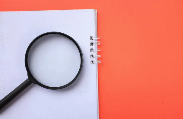 Magnifying glass  with notebook isolate on a orange background. Searching concept.