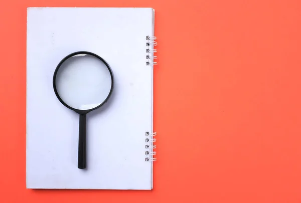 Magnifying glass  with notebook isolate on a orange background. Searching concept.