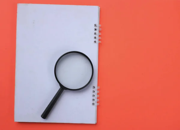 Magnifying glass  with notebook isolate on a orange background. Searching concept.