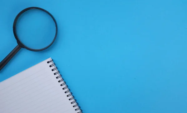 Magnifying glass  with notebook isolate on a blue background. Searching concept.