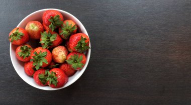 En üstte taze sulu çilekler ahşap masa üzerinde bir kasede, siyah arka planda.