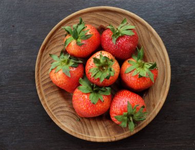 Tahta bir tabakta taze sulu çilekler, ahşap masa üzerinde siyah arka plan.