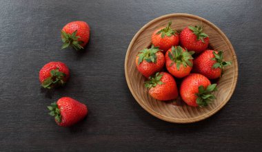 Tahta bir tabakta taze sulu çilekler, ahşap masa üzerinde siyah arka plan.